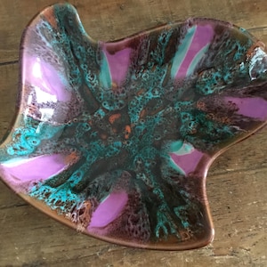 May include: An irregular, leaf-shaped ceramic dish featuring a glossy glaze with a vibrant color palette of bright pink, deep brown, and turquoise blue. The surface displays a mottled, textured pattern where the colors blend and overlap.