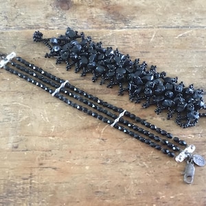 Peut inclure: Deux bracelets noirs. L'un est composé de trois rangs de perles noires à facettes reliées par des barrettes en métal argenté avec un fermoir mousqueton. Le second est un bracelet large formé de nombreuses perles noires irrégulières.