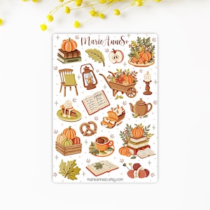 K&ouml;nnte beinhalten: Eine Bogen mit Aufklebern mit Herbstmotiven, darunter K&uuml;rbisse, B&uuml;cher, eine Schubkarre, eine Laterne, ein Kuchen, ein Brezel, eine Tasse Kaffee und Wolle. Die Aufkleber sind auf wei&szlig;em Hintergrund und haben einen verspielten, handgezeichneten Stil. Der Text "MarieAnneSo" und "marianneaso.etsy.com" ist auf dem Bogen enthalten.