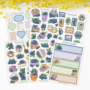 Peut inclure: Une collection de six planches d'autocollants illustrées sur le thème des myrtilles, incluant des tartes, des pancakes, des boissons et des éléments de papeterie. Chaque planche porte la marque MarieAnneSo et des motifs bleus, violets et verts.