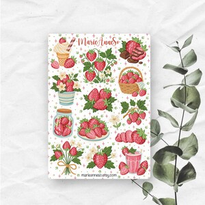 May include: A sheet of strawberry-themed stickers with various illustrations. The designs include strawberries, strawberry plants, ice cream, a basket of strawberries, and a jar of strawberries. The text "MarieAnneSo" and a website address are also visible.