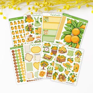 Peut inclure: Plusieurs planches d'autocollants décoratifs sur le thème des agrumes, avec des oranges, des citrons et des accents verts. Les autocollants comprennent divers motifs tels que des oranges sur des branches, une théière et une balance. Le texte "MarieAnneSo" est visible.