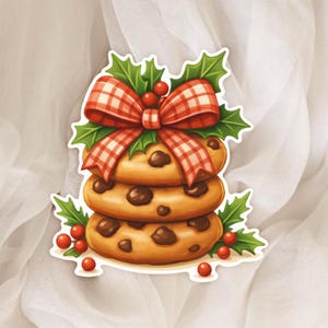 May include: A festive image of three chocolate chip cookies stacked high, decorated with a red and white checked bow, holly leaves, and red berries. The cookies are a golden brown colour and have chocolate chips.