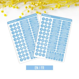 May include: Two rectangular sticker sheets featuring light blue labels with white text. One sheet contains English days of the week and numbers 1-31 in circles. The other sheet features French days of the week and numbers 1-31 in circles. Both sheets display the text marieannesa.etsy.com.