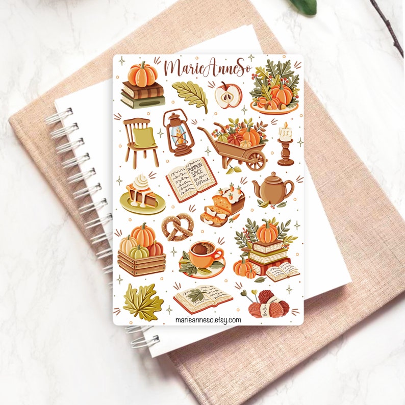 K&ouml;nnte beinhalten: Eine Bogen mit Aufklebern mit herbstlichen Illustrationen, darunter K&uuml;rbisse, B&uuml;cher, eine Schubkarre, eine Laterne, ein Kuchen, ein Brezel, eine Tasse Kaffee und Wolle. Die Aufkleber sind auf wei&szlig;em Hintergrund und haben eine verspielte, gem&uuml;tliche &Auml;sthetik. Der Text "Marie Anne So" und "marieannesoso.etsy.com" ist auf dem Bogen enthalten.