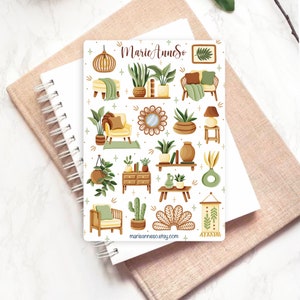 May include: A sheet of stickers featuring illustrations of home decor items in a boho style. The stickers include plants, furniture, lamps, and other decorative elements. The stickers are white with a light brown background and feature a variety of green, brown, and yellow colors.