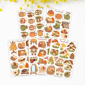 Può includere: Cinque fogli di adesivi con illustrazioni a tema autunnale tra cui tazze, zucche, funghi, ghiande, maglieria e oggetti per la casa. Ogni foglio riporta la scritta MarieAnneSo e mostra varie icone stagionali in colori caldi.