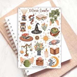 Puede incluir: Una hoja de pegatinas con varias ilustraciones que incluyen un difusor de varillas, un libro abierto, cartas del tarot, un reloj de arena, un sombrero de bruja, flores, una taza de t&eacute;, un sol, un planeta, una balanza, una vela, una bola de cristal y un rat&oacute;n sobre una luna creciente.