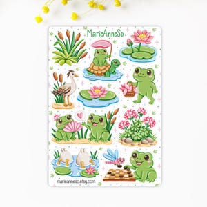 May include: A sticker sheet featuring various cartoon frogs in a pond setting. The frogs are depicted with lily pads, flowers, and other pond elements. The sticker sheet includes the text "MarieAnneSo." and "marieanneso.etsy.com".