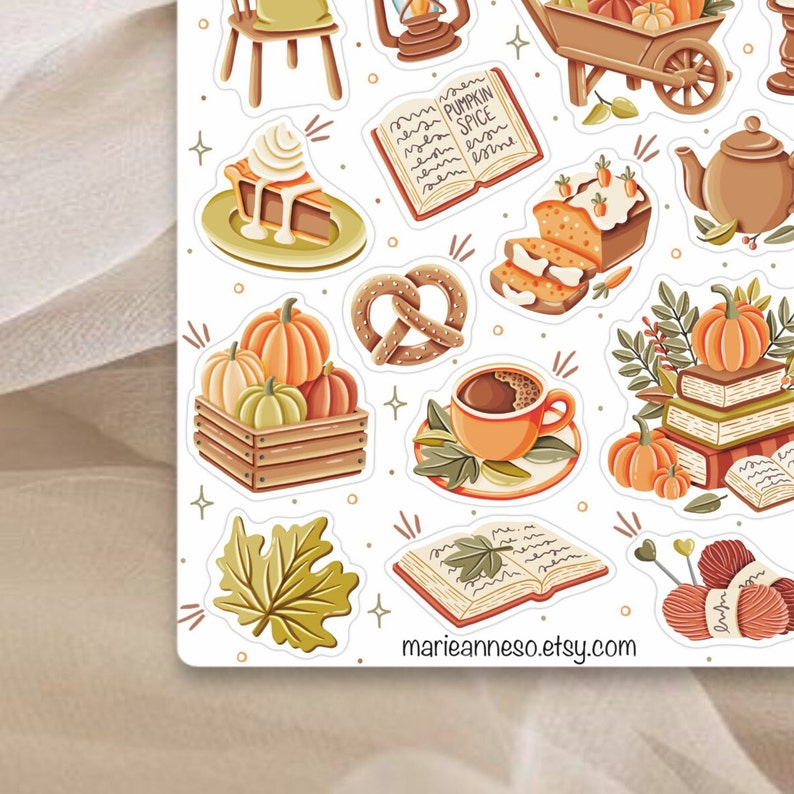 K&ouml;nnte beinhalten: Ein Set mit Herbst-Stickern mit K&uuml;rbissen, einem Buch, einer Kaffeetasse, einem Brezel, einem Kuchen, einem Brotlaib, einer Teekanne, einer Schubkarre, einer Laterne, einem Stuhl, einem Blatt und Wolle. Die Sticker sind auf wei&szlig;em Hintergrund.