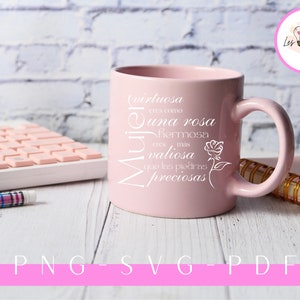 Op de afbeelding: Een roze keramische mok met een wit ontwerp met de tekst "Virtuosa eres como una rosa hermosa eres mas valiosa que las piedras preciosas" en een kleine roos afbeelding. De mok staat op een wit houten oppervlak met een toetsenbord en een pen.