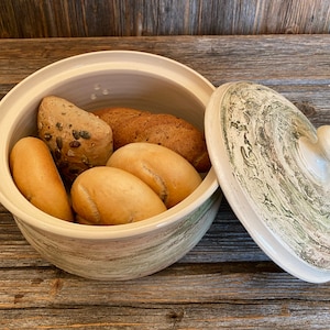 Könnte beinhalten: Ein Brotbehälter aus Keramik mit Deckel. Der Behälter ist mit einem grün-weißen Wirbelmuster verziert. Der Deckel hat einen Knopf oben. Der Behälter ist mit vier Brotstücken gefüllt.