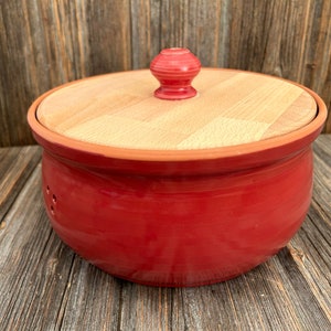 Op de afbeelding: Rode keramische broodtrommel met een houten deksel en een knop bovenop. Het deksel heeft een houtnerf.