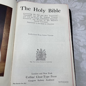 Puede incluir: Libro abierto titulado "The Holy Bible" con texto negro. La p&aacute;gina del t&iacute;tulo incluye el texto "Authorized King James Version" y la informaci&oacute;n del editor. El libro tiene un borde rojo y est&aacute; encuadernado en negro.