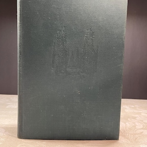 Puede incluir: Un libro de tapa dura verde oscuro con una cubierta texturizada. El libro tiene un diseño en relieve sutil en la parte delantera, posiblemente de árboles o un edificio. El libro está de pie sobre una superficie estampada.