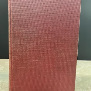 May include: A vintage book with a textured, reddish-brown cover. The spine shows signs of wear, suggesting age. The book's cover has a subtle, woven pattern, and the edges are slightly worn.