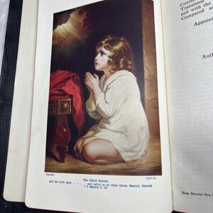 Puede incluir: Libro abierto con una ilustraci&oacute;n en color de un ni&ntilde;o arrodillado en oraci&oacute;n. El ni&ntilde;o lleva una prenda blanca. El texto debajo de la imagen dice "The Infant Samuel" y "And the Lord came...". El libro est&aacute; encuadernado en cuero negro.