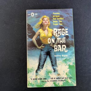 以下が含まれることがあります： ジェフリー・ワグナー著のヴィンテージペーパーバック『Rage on the Bar』。表紙には、黄色いノースリーブのトップスと青いジーンズを着て波の中に立つ金髪の人物のイラストが描かれており、情熱と陰謀についてのテキストが添えられています。
