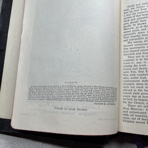 Puede incluir: Biblia abierta con texto visible en las p&aacute;ginas, incluyendo la palabra "Licence" y "Printed in Great Britain". El libro tiene una cubierta negra y bordes de p&aacute;gina rojos. Las p&aacute;ginas son de color blanquecino.