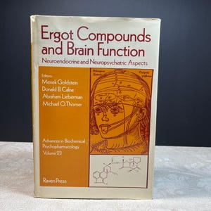 Op de afbeelding: Een hardcover boek getiteld Ergot Compounds and Brain Function: Neuroendocrine and Neuropsychiatric Aspects. De kaft heeft een crèmekleurige achtergrond met oranje accenten, een lijntekening van een menselijk hoofd en een chemisch structuurdiagram.