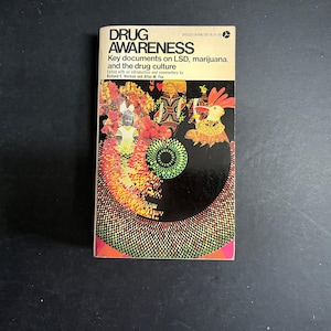 May include: A paperback book titled Drug Awareness: Key documents on LSD, marijuana, and the drug culture. The cover features a black background with a vibrant, multi-colored circular graphic pattern, a small figure of a child, and a rabbit illustration.