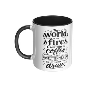 May include: White ceramic coffee mug with a black interior and handle. The mug features the text "The world is on fire but this coffee is the perfect temperature so let's call it a draw" in black script.