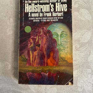 May include: A vintage paperback book titled "Hellstrom's Hive" by Frank Herbert. The cover features a surreal illustration with figures and a large face. The book is a science fiction novel, with text indicating it's by the author of "Dune".