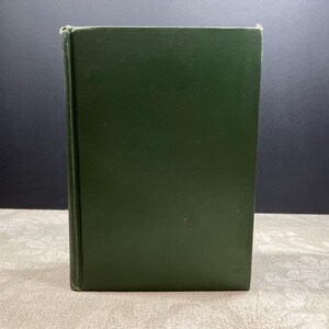 Pode incluir: Um livro de capa dura com uma capa verde escuro. O livro está em pé, com a lombada visível. A capa é de cor verde fosco sólido. O livro parece estar em bom estado, com desgaste mínimo. Provavelmente um romance.