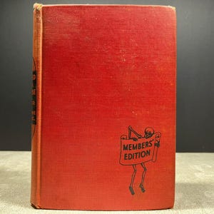 May include: A red hardcover book with a black graphic of a skeleton holding a banner that reads MEMBERS' EDITION. The spine features black text on a dark background. The cover has a textured fabric appearance with visible wear along the edges.