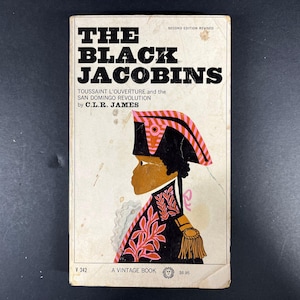 May include: A paperback book titled The Black Jacobins, Second Edition Revised, by C.L.R. James. The off-white cover features a stylized illustration of a figure in a black and pink military uniform and hat, with the text Toussaint L'Ouverture and the San Domingo Revolution.