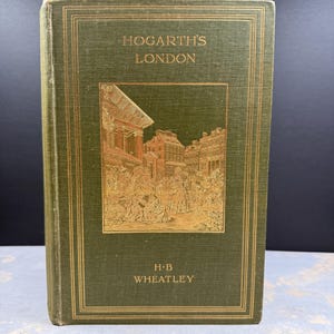 Könnte beinhalten: Ein Vintage-Buch mit dem Titel "Hogarth's London" von H.B. Wheatley. Das Buch hat einen dunkelgrünen Einband mit goldener Schrift und einer detaillierten Illustration einer Straßenszene. Das Buch ist in gutem Zustand.