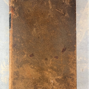 Puede incluir: Un libro encuadernado en cuero marrón desgastado con un lomo marrón oscuro.