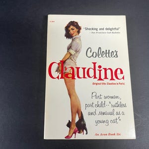 Pode incluir: Um livro de bolso vintage intitulado Colette's Claudine com uma capa branca apresentando uma ilustração de uma pessoa com roupas claras e saltos rosa ao lado de um gato preto. O texto inclui Shocking and delightful e An Avon Book 35c.