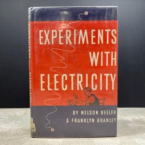 Könnte beinhalten: Ein Vintage-Buch mit dem Titel "Experiments With Electricity" von Nelson Beeler und Franklyn Branley. Das Cover ist rot mit weißem Text und einer stilisierten Illustration einer Person, die ein Experiment durchführt. Die oberen und unteren Abschnitte sind dunkelblau.