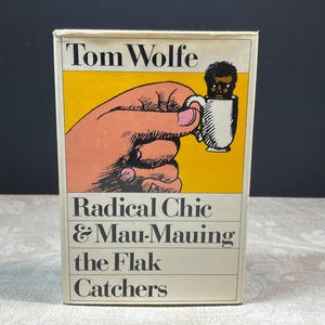 以下が含まれることがあります： トム・ウルフ著「Radical Chic & Mau-Mauing the Flak Catchers」というタイトルのヴィンテージ本。表紙には、顔が入ったマグカップを持つ手が、黄色の背景に描かれています。