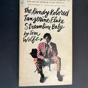 May include: A paperback book titled The Kandy-Kolored Tangerine-Flake Streamline Baby by Tom Wolfe. The cover features a person sitting on a chair, wearing a red and white striped blazer and red patterned pants, with text at the top reading VERDICT: Excellent book by a genius who will do anything to get attention. -Kurt Vonnegut, Jr. THE NEW YORK TIMES BOOK REVIEW.
