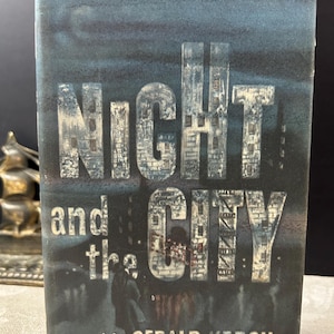 May include: A vintage book cover for "Night and the City" by Gerald Kersh. The cover features the title in large, textured letters against a dark blue background with a cityscape design. The author's name is at the bottom.