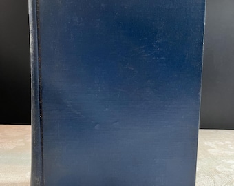 May include: A hardcover book with a navy blue cover. The book's cover has a textured, vertical lined pattern. The spine is a lighter shade of blue. The book is standing upright on a neutral-colored surface.