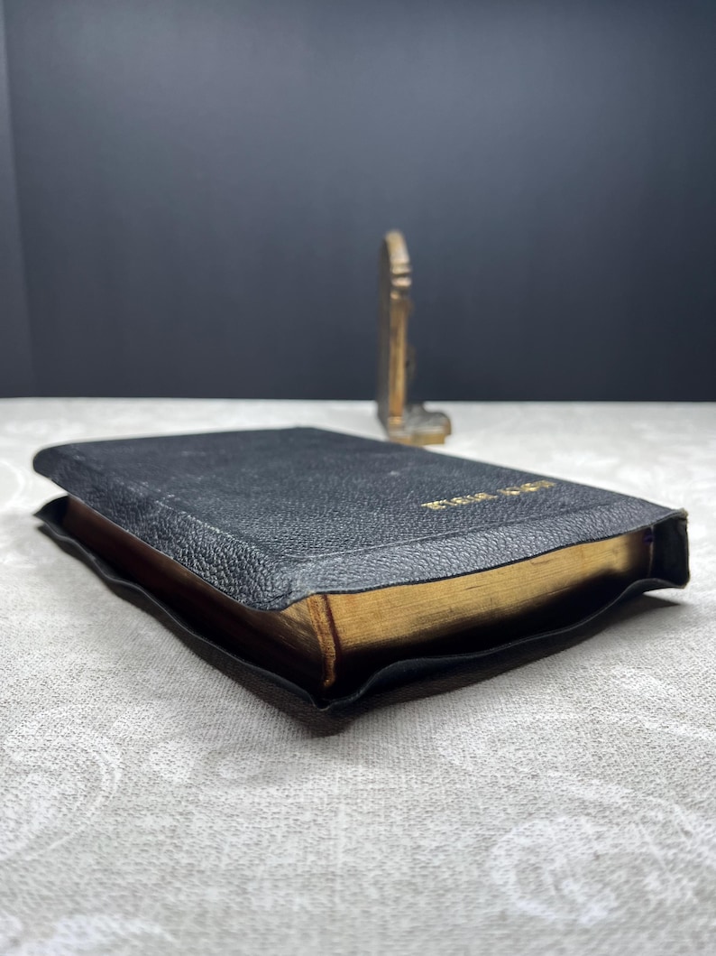 Puede incluir: Un libro encuadernado en cuero negro con bordes dorados. El libro est&aacute; abierto, revelando las p&aacute;ginas doradas. Un peque&ntilde;o objeto decorativo dorado est&aacute; en el fondo.