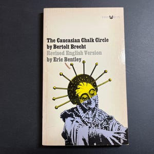以下が含まれることがあります： ベルトルト・ブレヒト著『The Caucasian Chalk Circle』、エリック・ベントレーによる改訂英語版のペーパーバック。表紙には、スパイク状のヘッドドレスと質感のある衣服を身に着けた人物の黄色と黒のグラフィックイラストが描かれています。