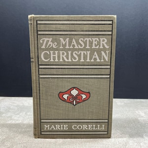 May include: A vintage book titled "The Master Christian" by Marie Corelli. The book has a tan cover with horizontal lines and a red and white emblem. The title is in a serif font.