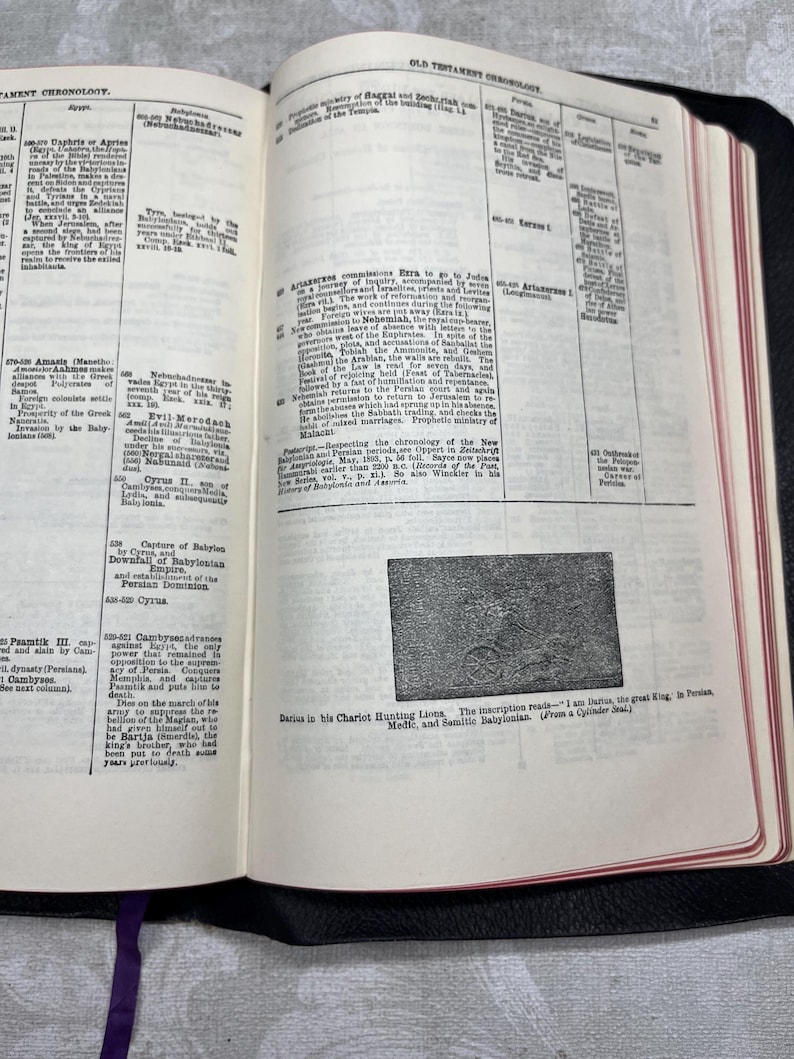 Puede incluir: Libro abierto con texto y una ilustraci&oacute;n. Las p&aacute;ginas son de color crema con texto negro y una peque&ntilde;a imagen de una escena de carro. El libro est&aacute; encuadernado en cuero negro con una cinta morada como marcador.