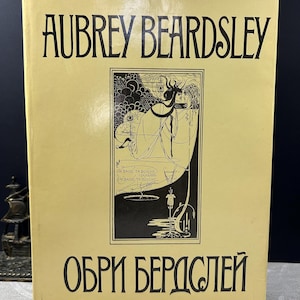 Peut inclure: Un livre vintage intitulé "Aubrey Beardsley" avec des lettres noires sur une couverture jaune clair. La couverture présente une illustration en noir et blanc et du texte en français. Le titre "ОБРИ БЕРДCЛЕЙ" est imprimé en noir en bas.
