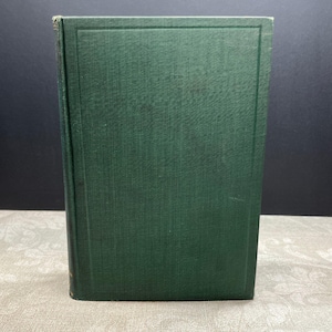 Puede incluir: Un libro de tapa dura verde oscuro, de pie. La cubierta tiene una textura y un borde rectangular. El lomo es visible. Probablemente sea una novela o un título de no ficción.