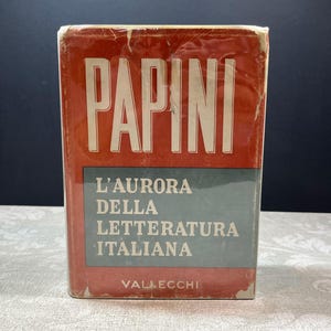 May include: A hardcover book with a red dust jacket featuring the white text PAPINI at the top, a grey rectangular center panel with the white text L'AURORA DELLA LETTERATURA ITALIANA, and the white text VALLECCHI printed at the bottom edge.