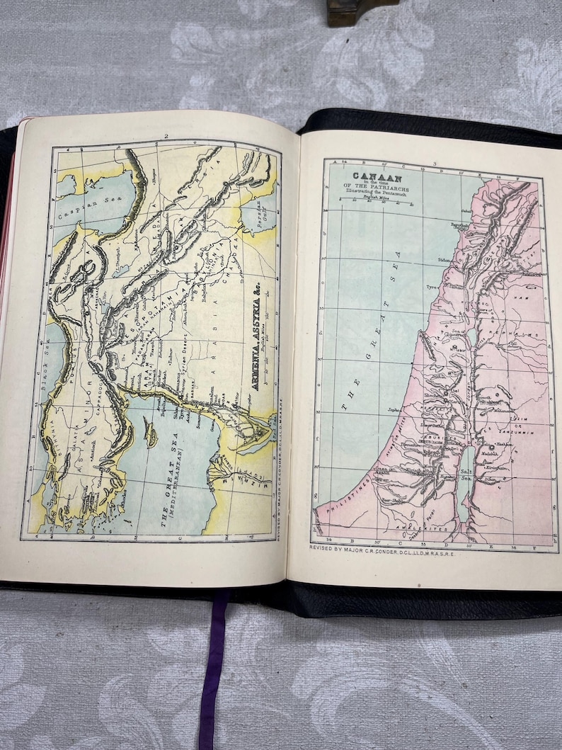 Puede incluir: Libro abierto con dos mapas antiguos detallados. La p&aacute;gina izquierda muestra un mapa de Armenia y Asiria, mientras que la p&aacute;gina derecha muestra un mapa de Cana&aacute;n. Ambos mapas est&aacute;n coloreados con tonos de amarillo, verde y rosa, con etiquetas de texto.
