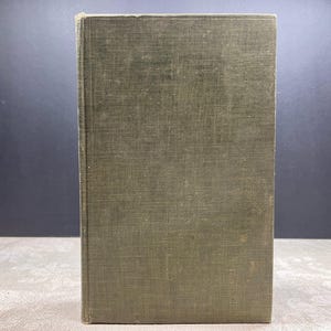 Puede incluir: Un libro antiguo con una cubierta texturizada de color verde oliva. El libro está de pie, mostrando su aspecto envejecido. La cubierta tiene un aspecto ligeramente desgastado, lo que sugiere que ha sido muy leído.