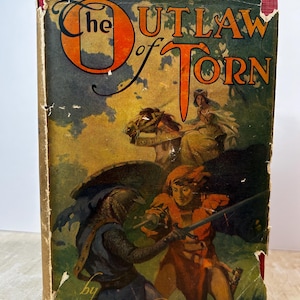 May include: The cover of a vintage book titled "The Outlaw of Torn" by Edgar Rice Burroughs. The cover features a colorful illustration of two men fighting with swords, one in red and one in blue, with a woman on horseback in the background.