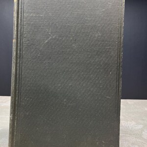 May include: An antique hardcover book with a dark green cover. The cover has a textured pattern and shows signs of wear. The spine is also green, with a slightly lighter shade. The book's edges are worn, suggesting age.