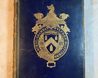 May include: A dark blue book with a gold embossed crest on the front cover. The crest features a shield with a gold design and the text "SCHOLAE GRAMMAT. WYLFREN. HANTVEN. 15 15".